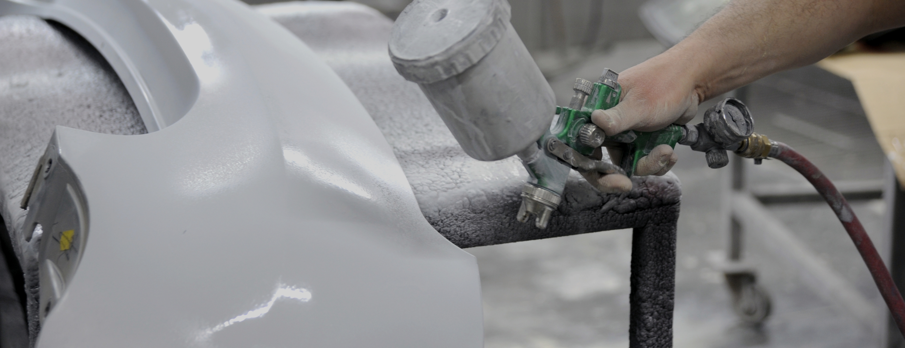 Aplikace automobilového laku stříkací pistolí v průmyslovém prostředí, ilustrující technická řešení testovaná přímo na výrobní lince.